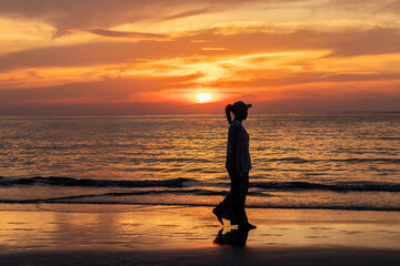 Happy young asian woman walking alone on a beach at sunset.