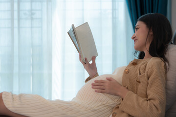 Pregnant woman reading a stories to her unborn child in the living room at home
