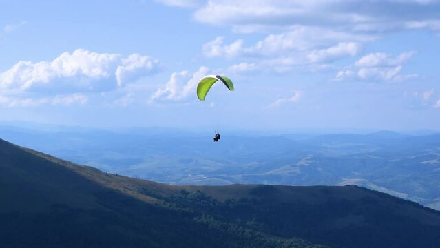 Paragliding instructor and a passenger are flying a paraglider in tandem. Beautiful summer sunny day. High mountain Carpathian landscape. Blue cloudy sky.