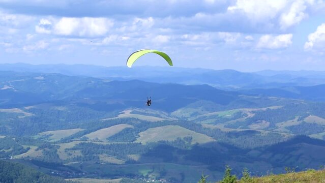 Paragliding instructor and a passenger are flying a paraglider in tandem. Beautiful summer sunny day. High mountain Carpathian landscape. Blue cloudy sky.
