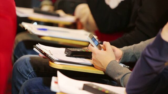 Hands of man holding mobile phone and notebook in auditorium