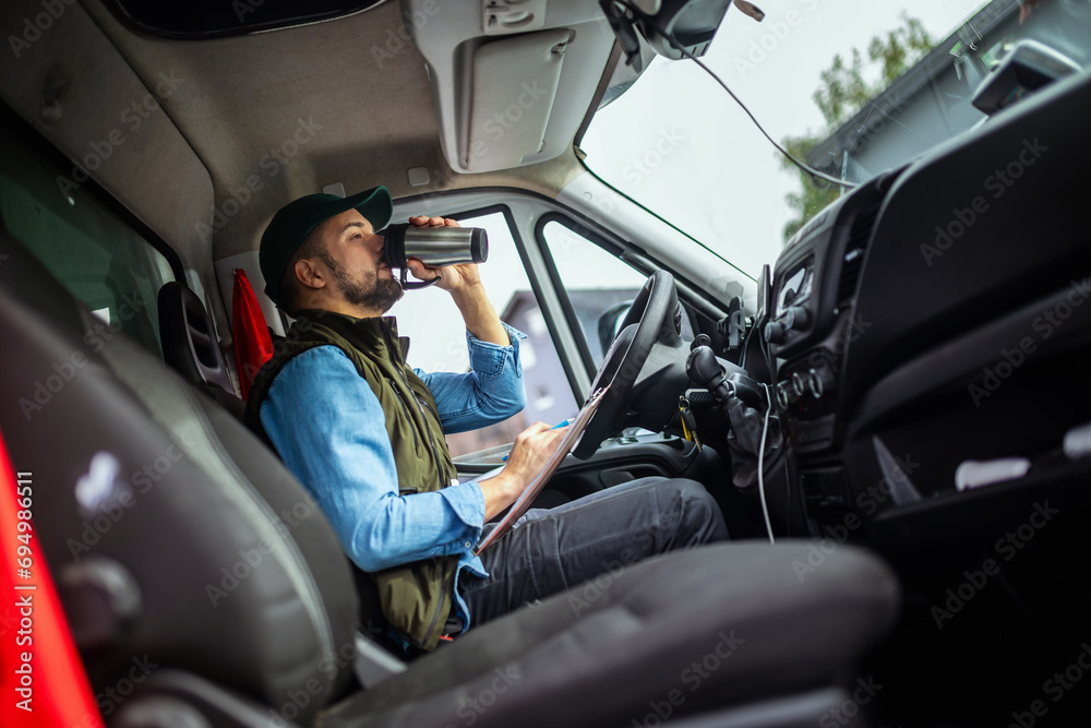 Wall mural Young handsome man working in towing service and drinking coffee so he could get some energy