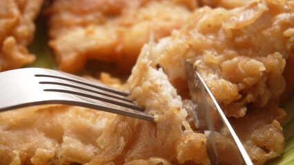 A fork lifts a flaky piece of fried fish, showcasing its crispy texture against more fillets in the background.