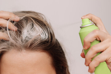 Woman's head with dirty greasy hair. The girl spraying dry shampoo on the roots of her hair on a light background. The problem of oily scalp. A quick way to cleanse - obrazy, fototapety, plakaty