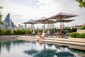 Woman relaxing at luxury rooftop pool with city skyline. Urban leisure and lifestyle.