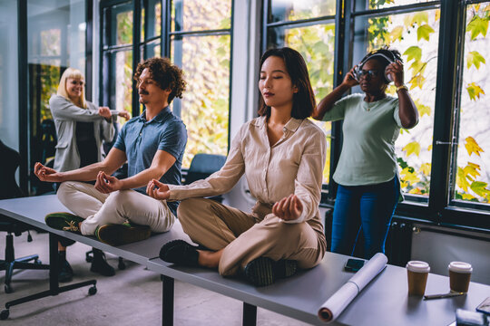 Young Business People Doing Relaxation Exercises At Casual Office. Meditation In Office. People Listening To The Music In The Background.