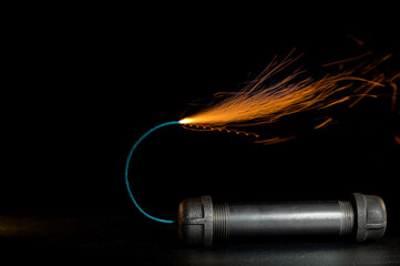 A metal pipe bomb with lit fuse against a black background