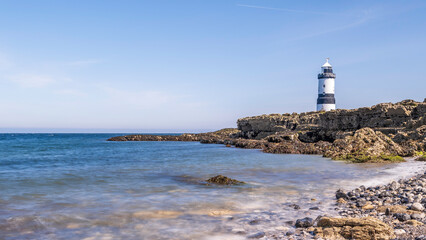Lighthouse on the edge of a rocky headland.  The lighthouse is located at Penmon Point, Angelsey, north Wales. The day is sunny