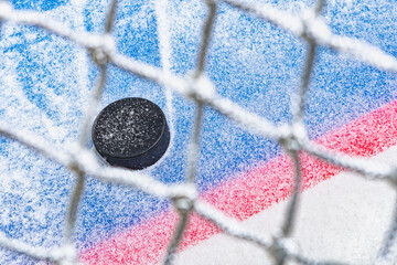 Looking through the net at an ice hockey puck stopping on the edge of the Goal Line of the goal crease.