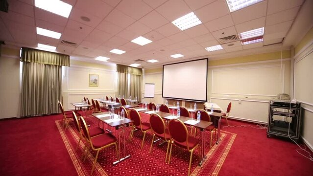 Screen for projector, tables and red chairs in meeting hall