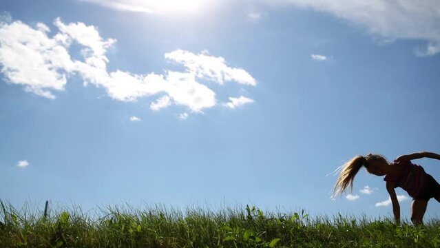 Little girl in shorts turns cartwheel on green grass