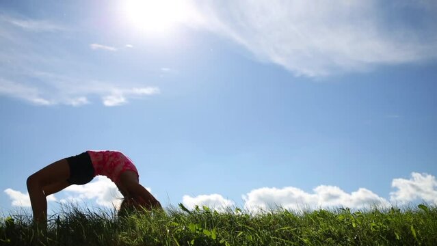 Little girl in shorts does exercise Bridge on green grass