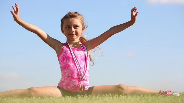 Little girl in shorts splitting legs apart on green grass 