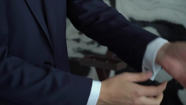 A close up of hands buttoning a suit. Man put on black jacket. Groom in wedding day or businessman. Male in white shirt indoors.