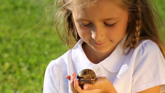 Portrait of smiling little girl with large snail in hand outdoor