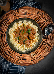 Pasta with beef stew in black bowl.