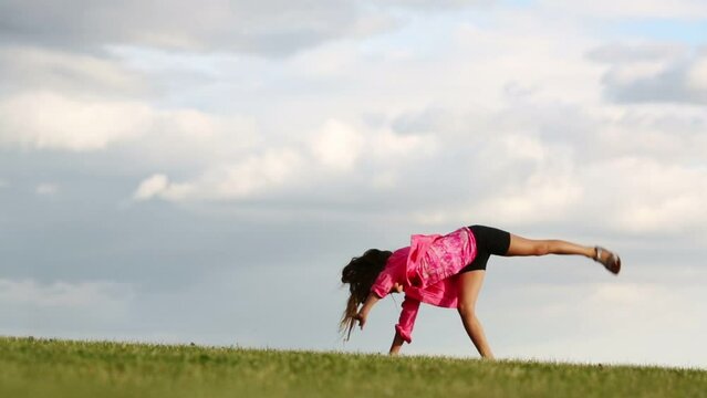 Little girl in pink does cartwheel at green meadow