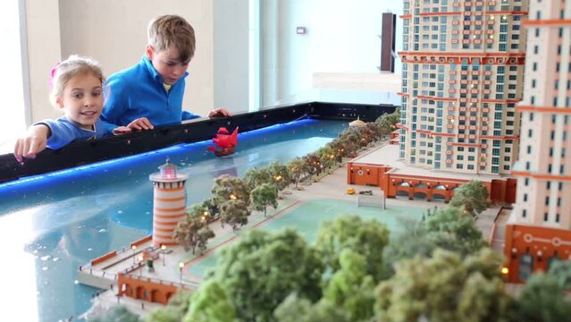 Boy and girl look at layout of buildings with river 