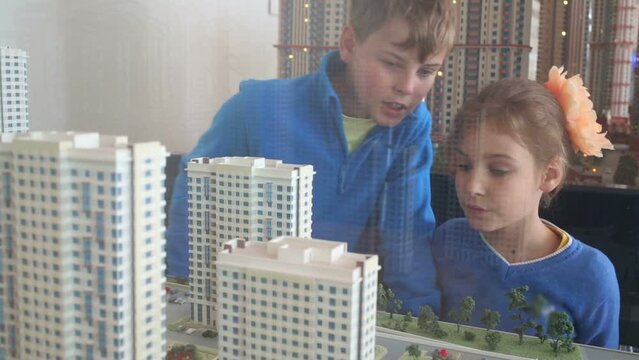 Talking boy and girl look at layout of buildings through glass