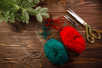 knitting needles, scissors and red and green yarns on wooden table decorated with spruce branches....