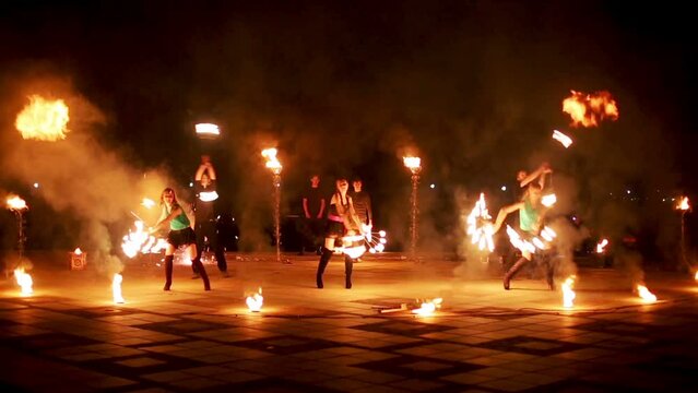 Group of firedancers dance, boy jumps making fireball.