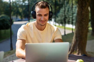 Guy in headphones working on laptop and looking contented