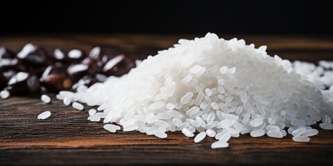 Heap of white rice spills softly onto the dark wood surface.