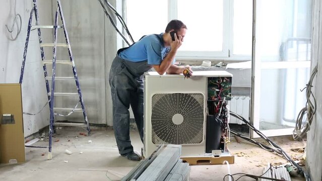 Worker sets air conditioner in apartment and talking on phone