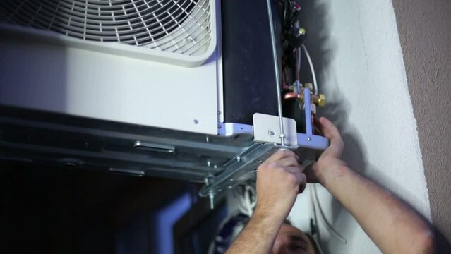Young serious worker sets split system air conditioner outdoor 