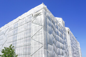With white safety net covered multistorey residential building facade during renovation works