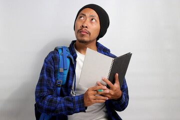 A pensive young Asian student, dressed in a beanie hat and casual shirt, carrying a backpack and holding a notebook, is engrossed in tackling a challenging assignment, deep in thought, exploring ideas