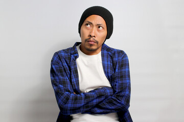 An angry, offended young Asian man stands with his arms folded, displaying an unsatisfied or...