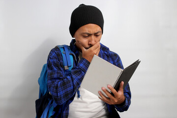 A pensive young Asian student, dressed in a beanie hat and casual shirt, carrying a backpack and...