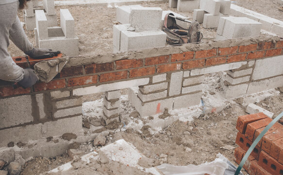 Bricklayer laying brick on cement mix on construction site close-up. Reduce the housing crisis by building more affordable houses concept