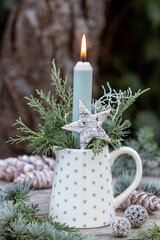 Weihnachtsdekoration mit einer Kerze und Koniferenzweigen im Milchkännchen im Garten
