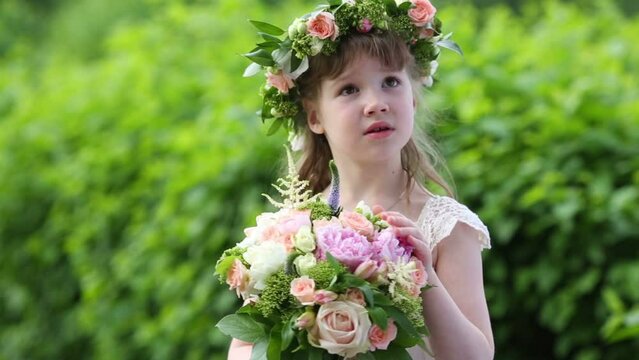 Little pretty girl in white dress and wreath touches bouquet