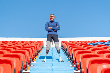 Sport man athlete prosthesis legs stand with arm crossed on stairs with happiness also look at camera on amphitheater in the stadium with day light.