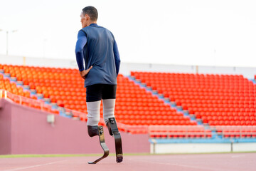 Back of Sport man athlete prosthesis legs walk in the track of the stadium with day light.