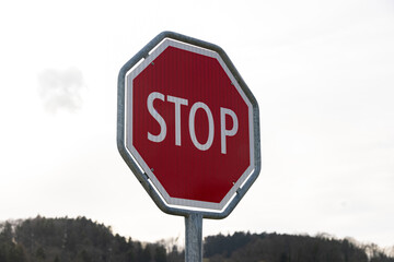 Red and white stop sign in front of a gray sky with forest, close up view, photographed from the left side, without people during the day