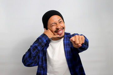 Excited young Asian man, dressed in a beanie hat and casual shirt is enthusiastically making a CALL...