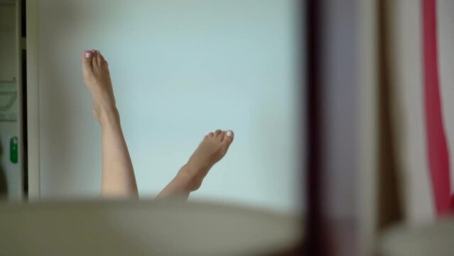 Woman laying in bed raise her naked legs up. Feet reflection in a mirror.