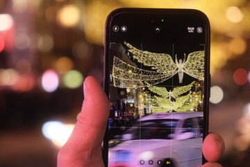 Close-up of a mobile phone photographing the Christmas lights on Regent's Street at night.