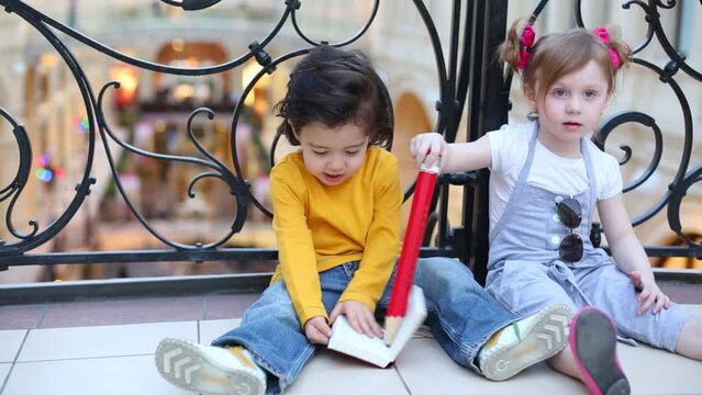 Little boy and girl sit on floor and draw in notebook by pencil