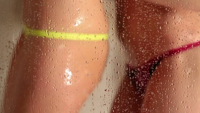 Two sexy girls in lingerie dancing at shower behind wet glass