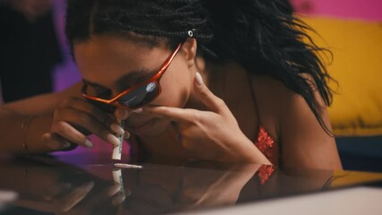 Close-up of young woman inhaling white powder using a dollar bill during a party - Powered by Adobe