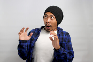 Excited young Asian man, dressed in a beanie hat and casual shirt, loudly exclaims WOW, his hands...