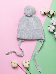 Gray children's knitted hat and decorative cotton branches on a colored paper background, top view