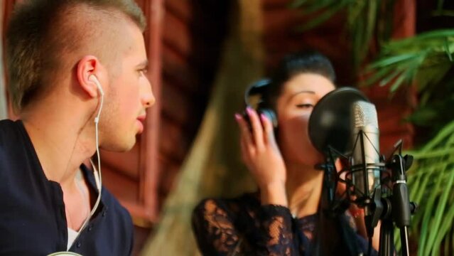 Young woman sings in microphone near man with earphones