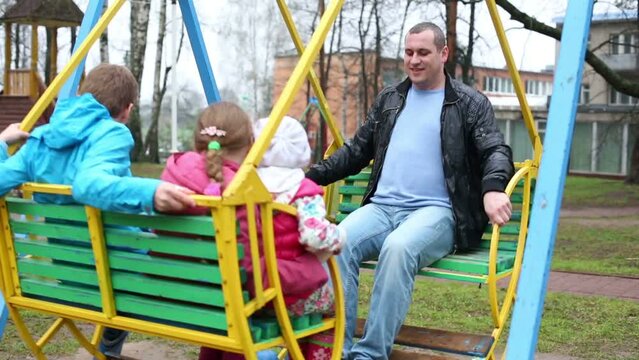 Happy father and three children on swings at playground