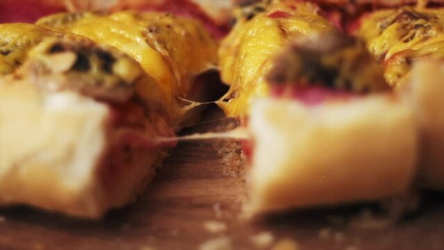 Close up of cut hot baked sandwich or bread boat with salami, champignon mushroom, tomato and cheese on wooden board. Slow motion